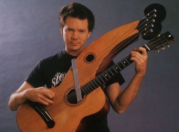 Michael posing with harp guitar on gray background